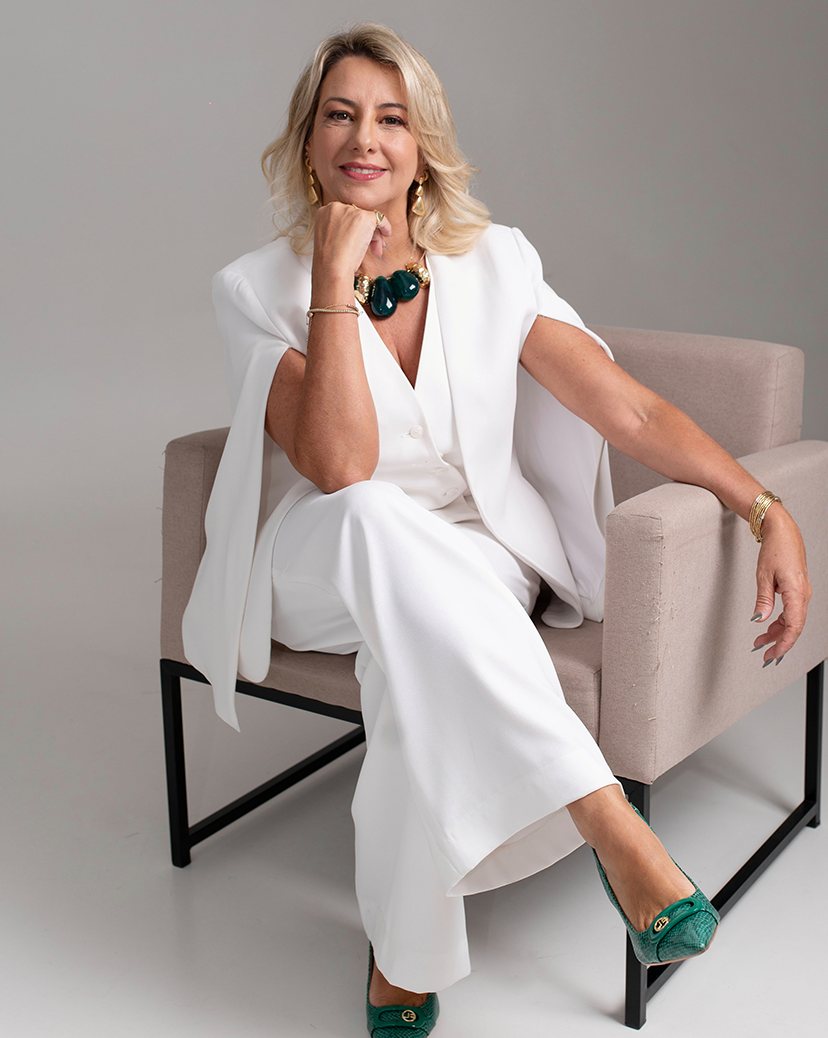 Dra. Adriane Bramante sentada em uma poltrona, de terninho branco